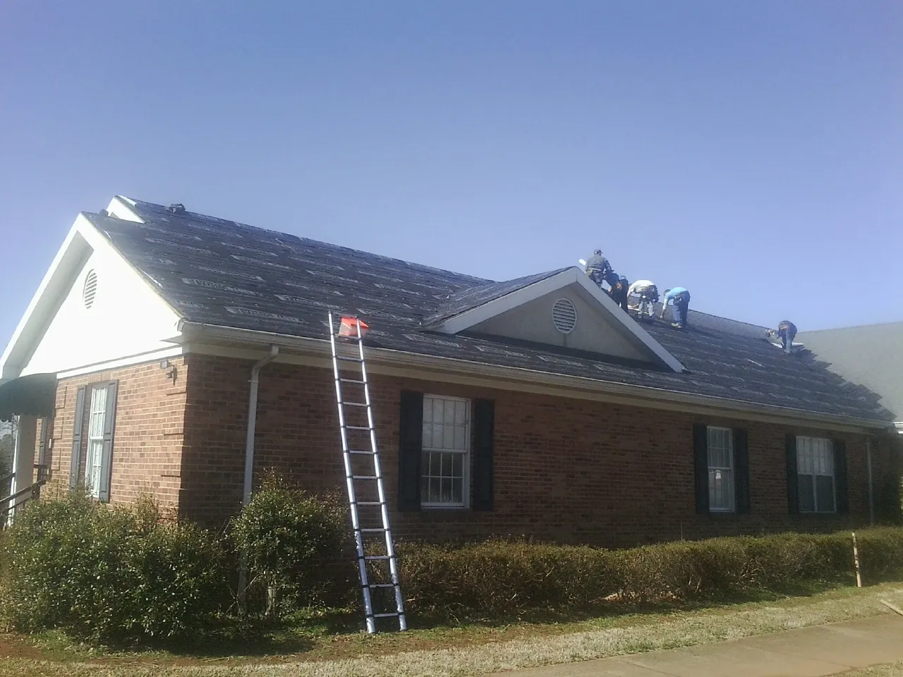 Crew tearing shingles off a brick ranch roof with a ladder set — Metal Roof Repair work by our crew in Rocky Top
