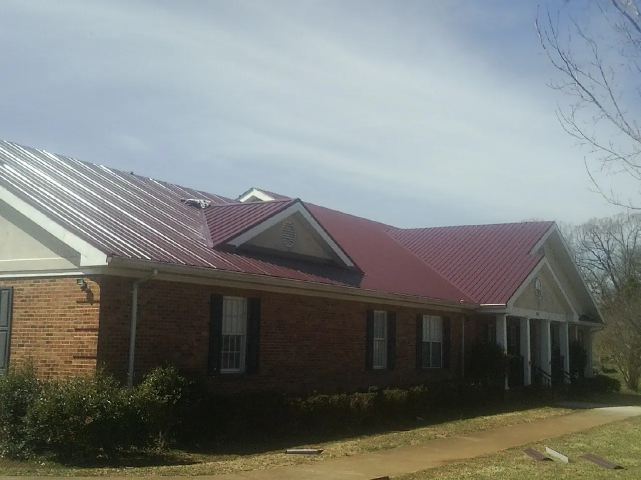 Red metal roof with gabled entries on a long brick building, from a Hail Damage Roof Repair job in Rocky Top