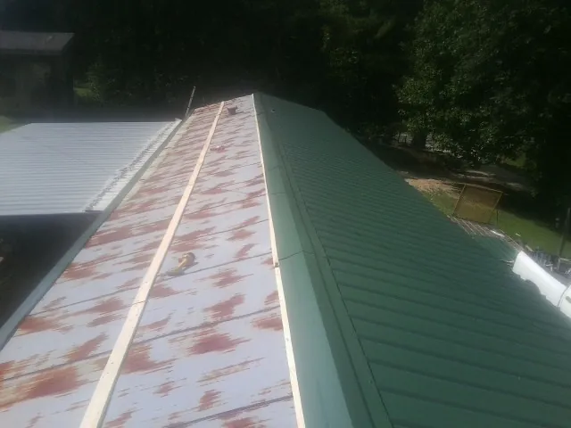 Old rusted panels beside newly installed green metal roofing — Wind Damage Roof Repair by Roofing Brothers in Rocky Top