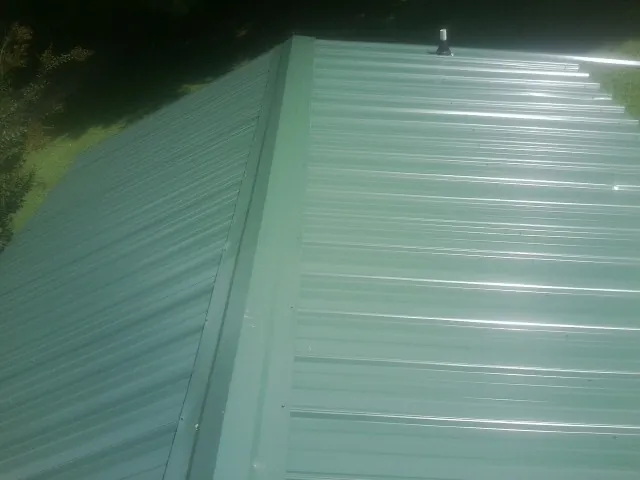 New green metal panels meeting at the ridge of a roof — Flat Roof Repair work by our crew in Rocky Top