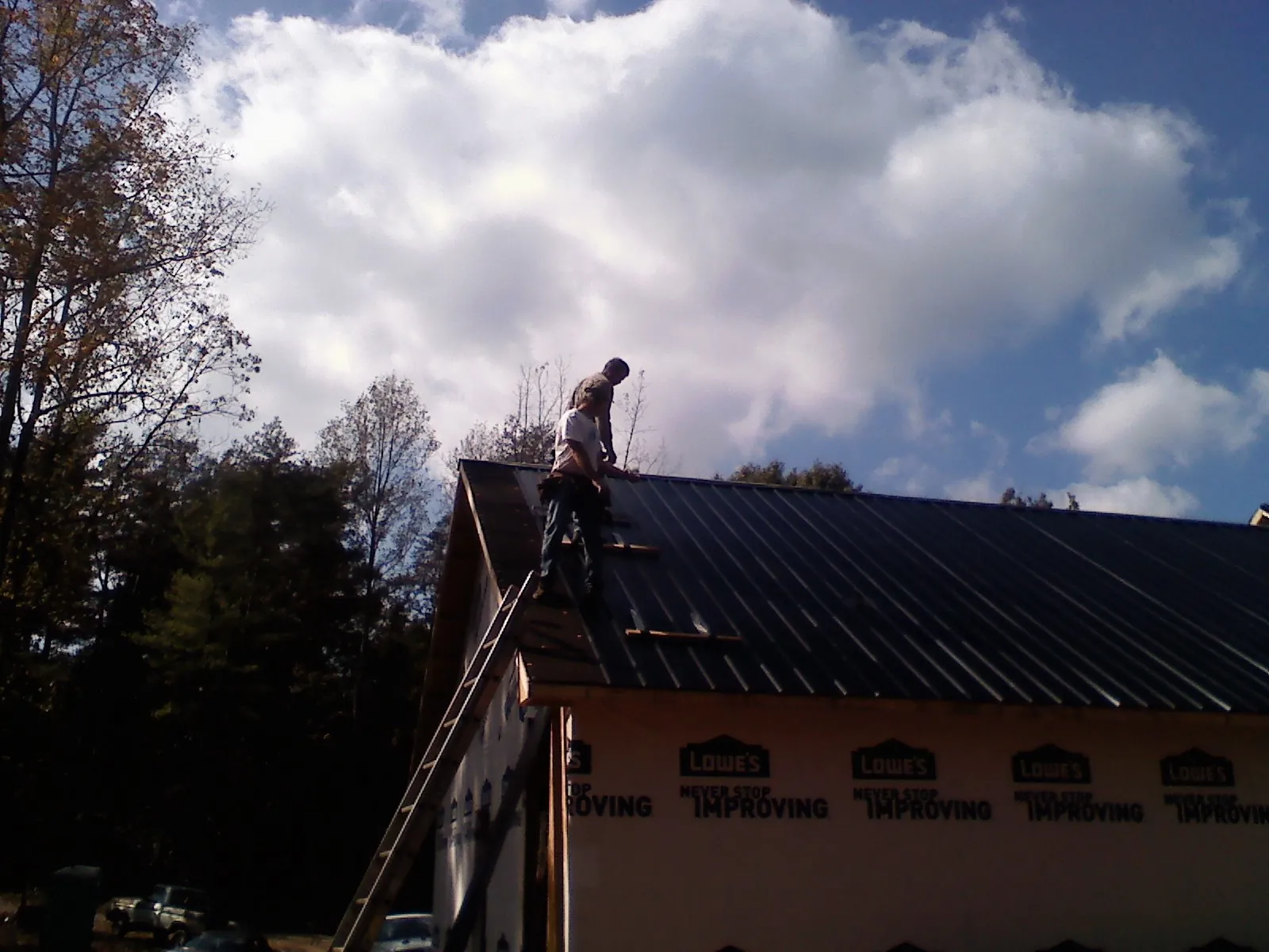 Roofer fastening dark metal panels high against a cloudy sky, from a Roof Inspection job in Rocky Top
