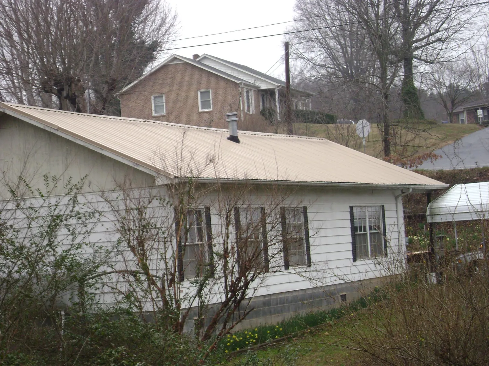 Tan metal roof on a white sided house set into a hillside — Commercial Roofing by Roofing Brothers in Rocky Top
